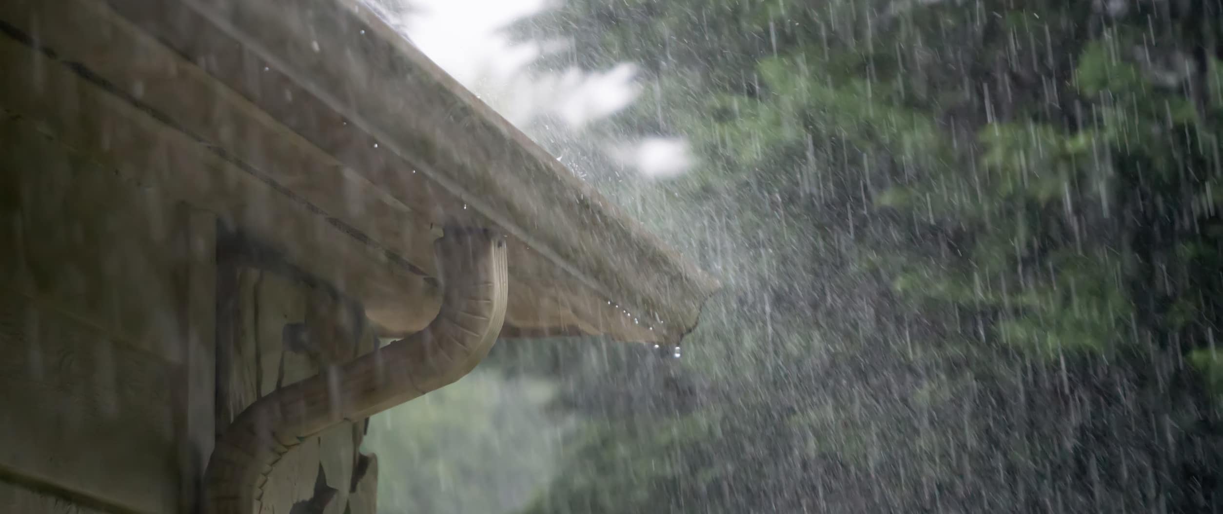 Rain pouring onto a home roof and gutter